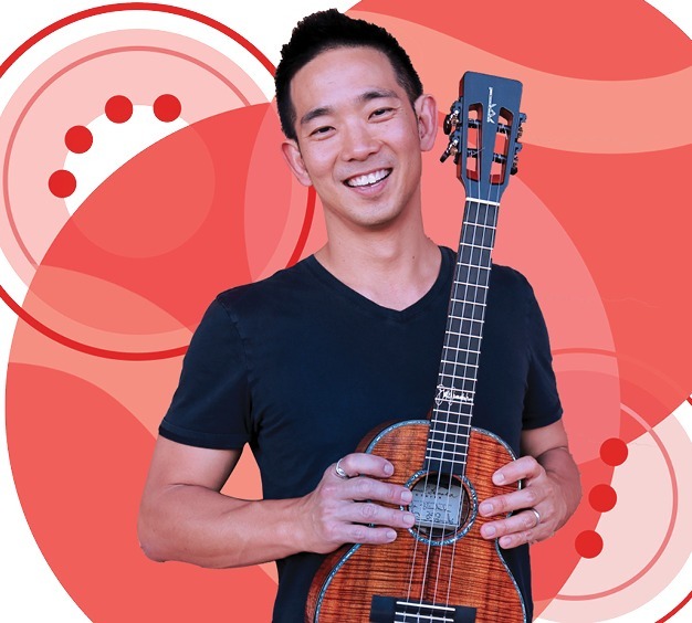 Jake Shimabukuro holding his ukulele in front of AARP branded background